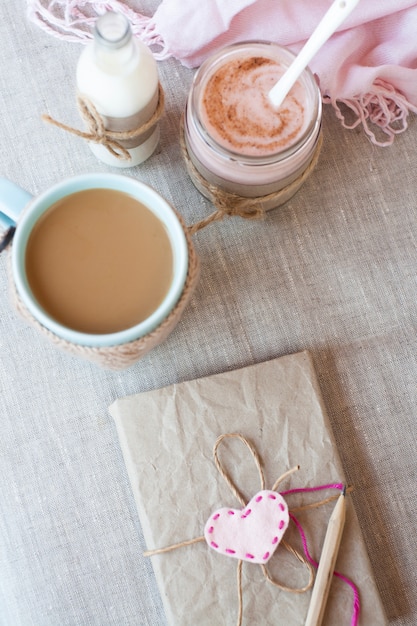 Flocons d'avoine, aromatisés au yaourt, saupoudrés de cannelle dans un bocal en verre. Vient ensuite une tasse de café et une bouteille de lait. Vient ensuite un carnet de bricolage et une serviette rose.