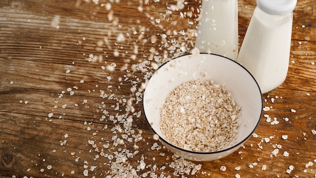 Flocons d'avoine dans un bol blanc et des bouteilles de lait frais. Fond rustique en bois