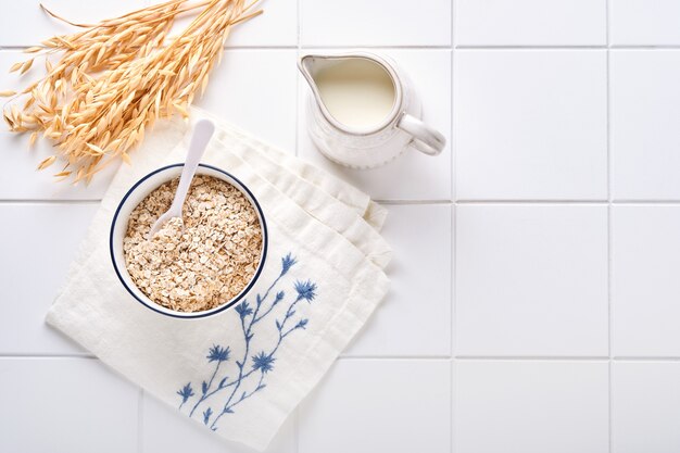 Flocons d'avoine dans un bol en bois et un pot de lait sur une table de cuisine en pierre blanche. Le concept d'un régime végétarien. Vue de dessus avec fond.