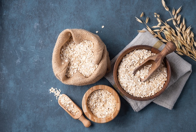 Flocons d'avoine dans un sac et un bol avec une cuillère en bois sur la table en bois bleu foncé