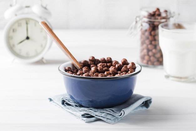 Flocons de cacao ronds dans une assiette avec une tasse de lait et un réveil en arrière-plan petit-déjeuner sec