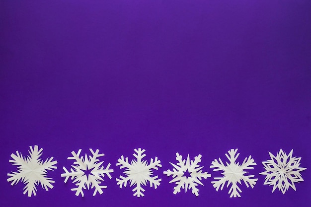 Flocons de neige en papier blanc de différentes formes et tailles sur fond violet Vue de dessus