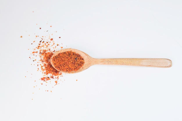 Flocons de piment rouge sur une cuillère en bois sur fond blanc