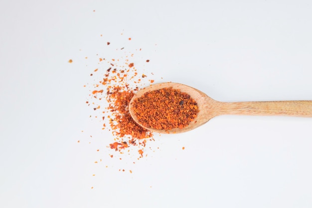 Flocons de piment rouge sur une cuillère en bois sur fond blanc