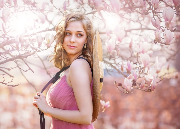 Photo floraison printanière portrait d'une jeune fille blonde dans les branches d'un magnolia en fleurs ouverture ouverte avec flou lumineux et illumination printemps