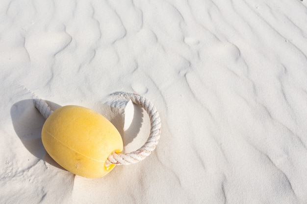 Flotteur jaune avec corde allongé sur la plage de sable blanc