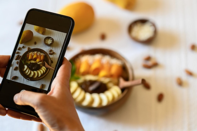 Photo flou artistique à grand angle d'un blogueur anonyme prenant une photo sur un smartphone d'un délicieux bol avec des fruits sucrés pour les médias sociaux