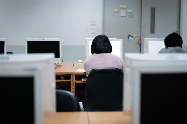 Flou et mise au point sélective des apprenants universitaires adultes portant un masque facial tout en se concentrant sur l'examen en ligne dans la salle informatique. Étudiants sérieux travaillant sur ordinateur à l'université