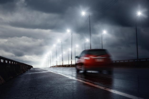 Flou de voiture roulant rapidement sur le pont pendant une pluie battante avec des nuages d'orage en arrière-plan