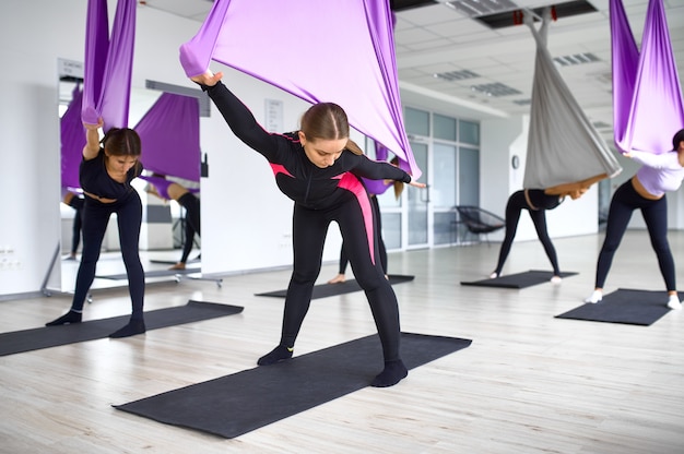 Fly yoga, formation de groupe de femmes avec des hamacs. Des exercices de fitness, de pilates et de danse se mélangent. Femmes sur entraînement yogi en studio de sport