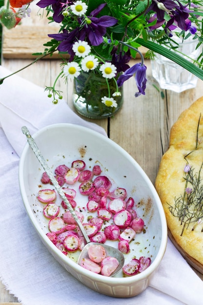 Focaccia aux oignons, radis au four et bouquet de fleurs sur une table en bois