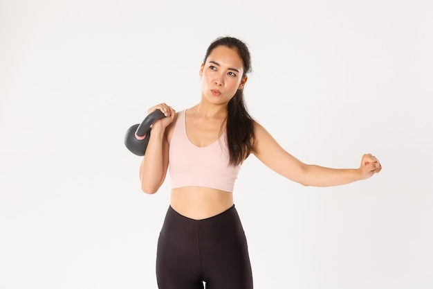 Focalisé asiatique fort poids de levage gitl dans la salle de gym, entraînement à domicile avec kettlebell, contrôle de la respiration pendant les exercices de fitness