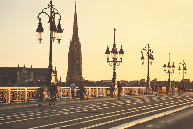 Photo focus sélectif sur la cathédrale saint michel, les gens à vélo sur le pont pont de pierre à bordeaux pendant le coucher du soleil