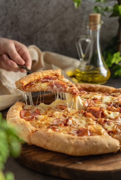 Focus sélectif pizza chaude avec du fromage et du pepperoni la fille tire une tranche de pizza avec du fromage fondu s'étendant en position verticale humeur sombre