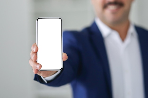Focus sélectif sur un smartphone avec un écran blanc vide tenu par un homme d'affaires en costume bleu
