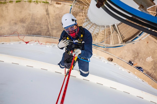 Focus vue de dessus travailleur masculin vers le bas hauteur réservoir toit corde accès inspection de sécurité de l'épaisseur du réservoir de stockage de gaz