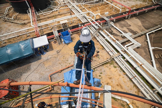 Focus vue de dessus travailleur masculin vers le bas hauteur réservoir toit corde accès inspection de sécurité de l'épaisseur du réservoir de stockage de pétrole brut