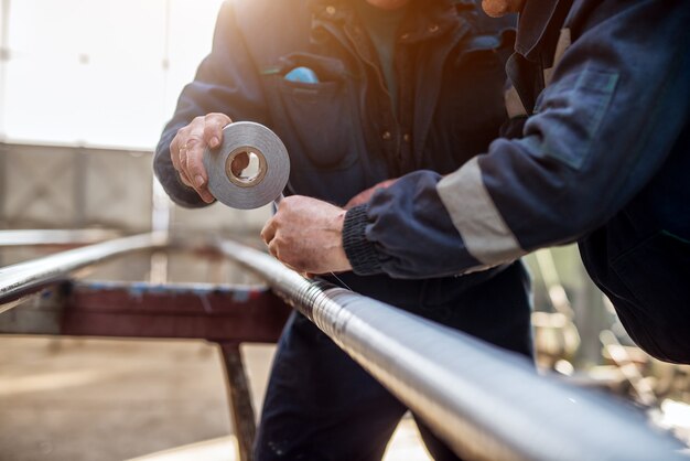 Focus vue de la main des travailleurs industriels professionnels en tuyau métallique de liaison uniforme avec du ruban adhésif.