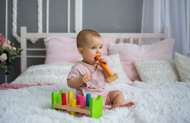 Focused baby girl est assis sur le lit avec un jouet éducatif coloré