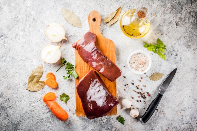 Foie de boeuf cru aux épices, herbes et légumes, vue de dessus de table en pierre grise