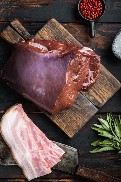 Foie de boeuf cru avec pancetta sur fond de bois, pose à plat.