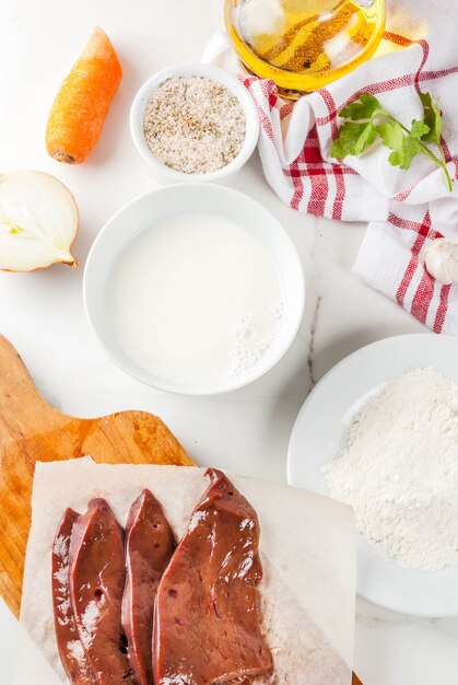 Foie de boeuf cru en tranches avec des épices, des herbes, du lait et de la farine, vue de dessus de table en marbre blanc