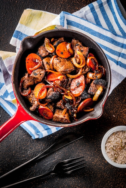 Foie de boeuf rôti ou grillé avec oignon et carotte dans une poêle à frire, vue de dessus de table rouillé foncé