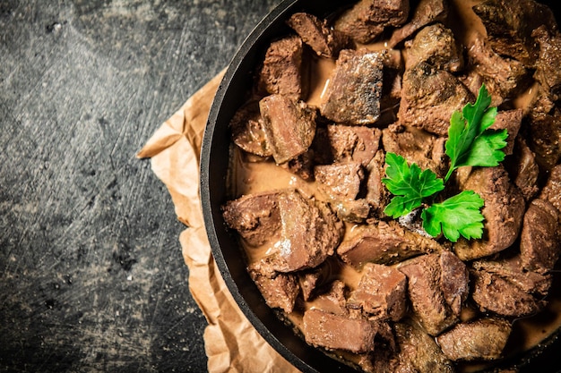 Le foie dans une poêle à frire sur papier avec une brindille de persil