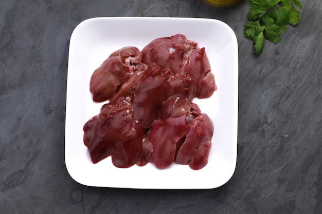 Foie de poulet cru magnifiquement disposé dans une assiette en céramique blanche