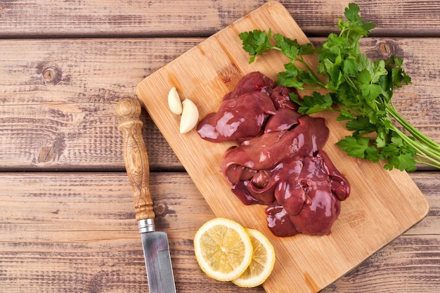 Foie de poulet cru sur une planche en bois, joliment servi avec du poivre, du citron et des herbes