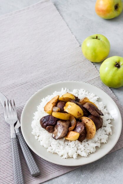 Foie de poulet frit aux pommes servi avec du riz blanc sur une assiette. Pommes vertes en surface. Copier l'espace