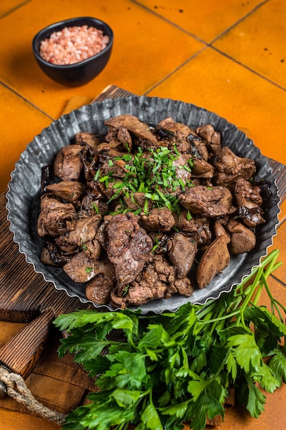 Foie de poulet rôti aux oignons et aux herbes dans une plaque d'acier Fond orange Vue de dessus