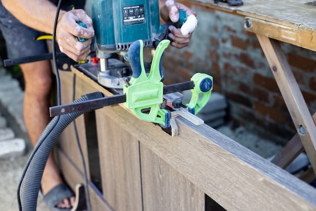 Fonctionne de manière dense avec une fraiseuse sur la surface en bois de la porte. Outils professionnels pour le travail du bois.