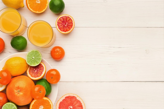 Fond d'agrumes. Assiette de fruits assortis et deux verres de jus de fruits frais sur des planches de bois blanches. Mode de vie sain, concept de vitamines naturelles, vue de dessus, espace de copie, mise à plat du blogueur