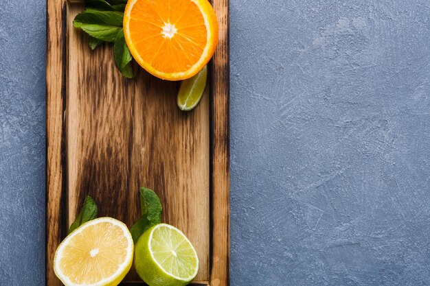 Fond d'agrumes. Composition juteuse d'oranges tranchées, de citrons, de citron vert et de menthe sur une planche de bois rustique sur une vue de dessus de table grise avec espace de copie. Faire du jus ou un smoothie détox et manger le bon concept