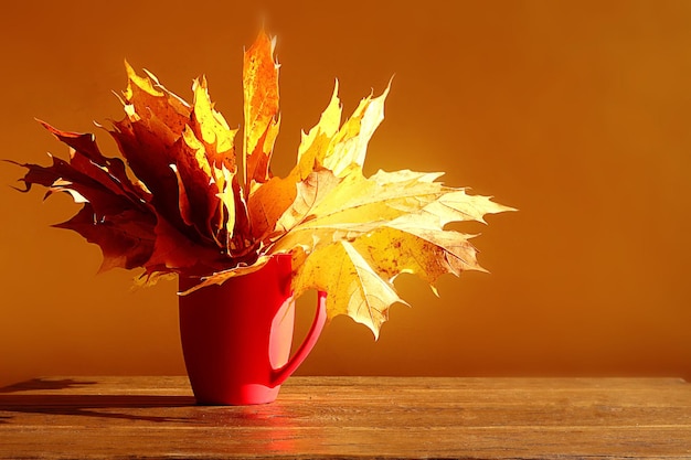 Fond d'automne un bouquet de feuilles d'automne dans une tasse rouge sur fond marron au soleil espace pour le texte