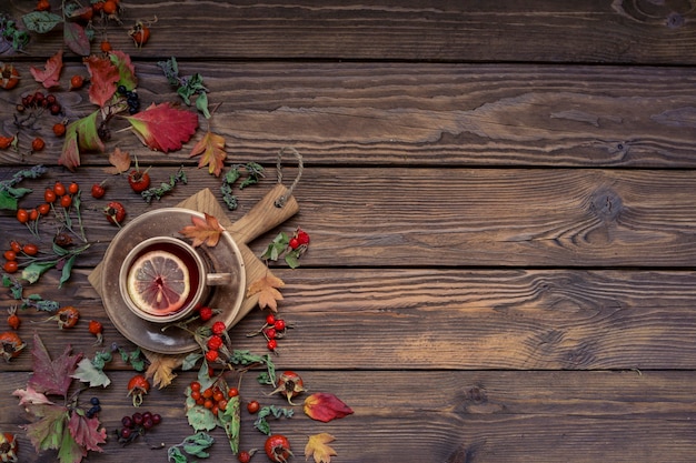 Fond d'automne avec espace de copie. Thé au citron, feuilles et baies sur une table en bois.