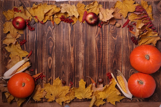 Fond d'automne avec des feuilles d'érable jaunes, des citrouilles, des pommes rouges et des baies. Cadre de récolte d'automne sur bois vieilli avec espace de copie. Maquette pour les offres saisonnières et carte postale de vacances, vue de dessus.