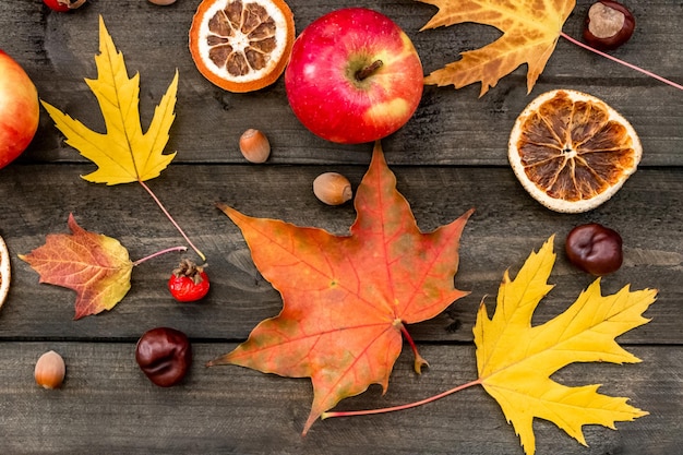 Fond d'automne feuilles d'érable pommes églantier noix châtaignes oranges séchées sur une table en bois