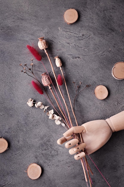 Fond d'automne avec des plantes sèches dans la main en bois Modèle de main en bois artistique Plantes de queue de pavot et de lapin avec eucalyptus sec et cercles en bois Vue de dessus à plat sur fond texturé sombre