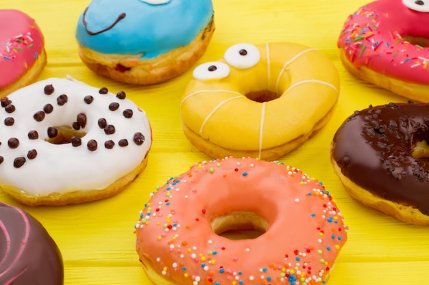 Fond de beignets glacés multicolores. Délicieux gâteaux givrés sur une surface en bois de couleur.