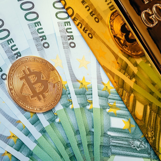 Sur le fond des billets en euros, un grand lingot d'or brillant et une pièce de monnaie bitcoin.