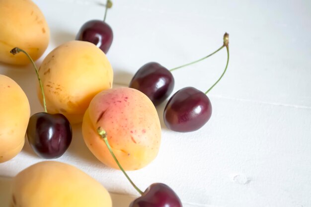 Sur fond blanc abricots et cerises Cerises lumineuses à côté d'abricots orange sur la table fruits et baies d'été