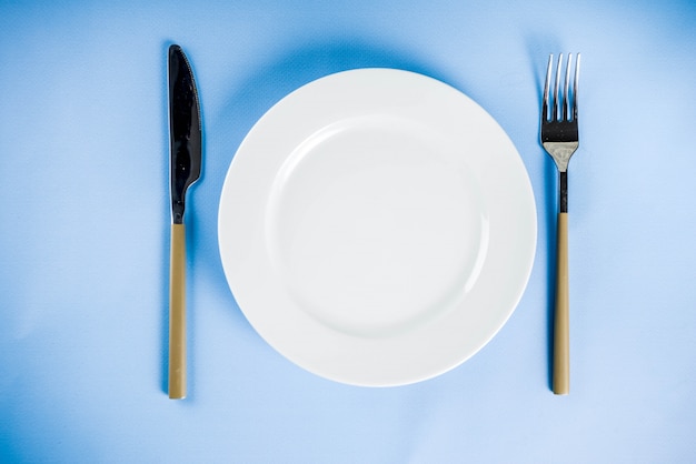 Fond bleu avec une assiette, une fourchette et un couteau, vue de dessus copie espace