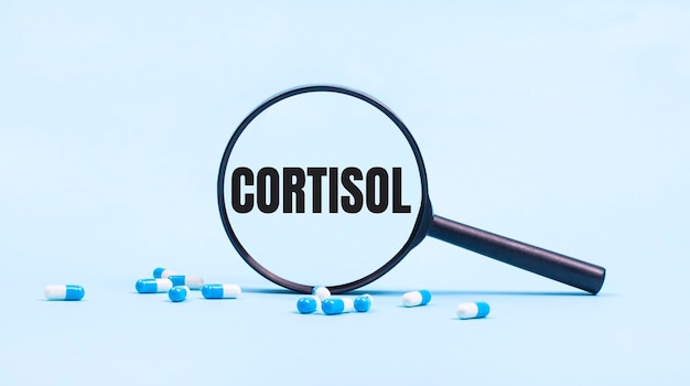 Sur un fond bleu capsules blanches et bleues avec des pilules et une loupe noire avec le texte CORTISOL Medical concept