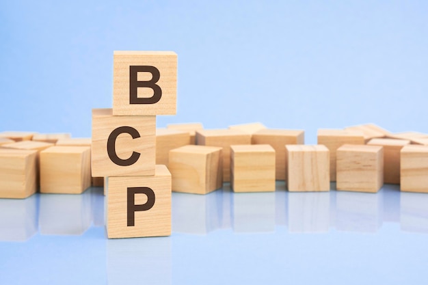 Sur un fond bleu clair, des blocs et des cubes en bois clair avec le texte BCP