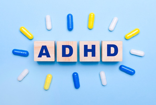 Sur fond bleu clair, pilules multicolores et cubes en bois avec le texte TDAH. Notion médicale