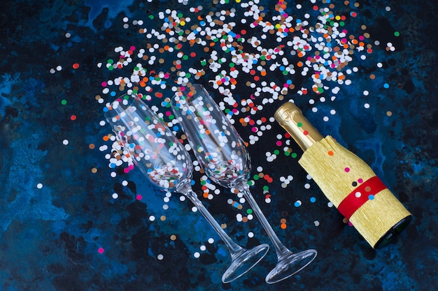 sur fond bleu foncé, deux verres de champagne, une bouteille de champagne et des confettis