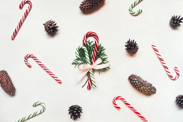 Fond en bois blanc avec des bonbons de Noël rouges et verts et des cônes de conifères