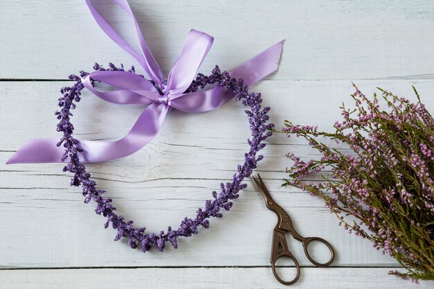 sur un fond en bois blanc coeur violet composé de fleurs violettes, ciseaux et une bruyère b